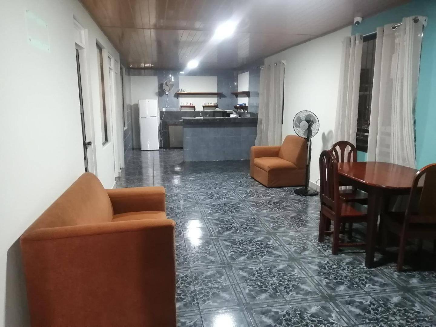 A bright apartment with tiled floor, sofa, dining table and a kitchen in the back