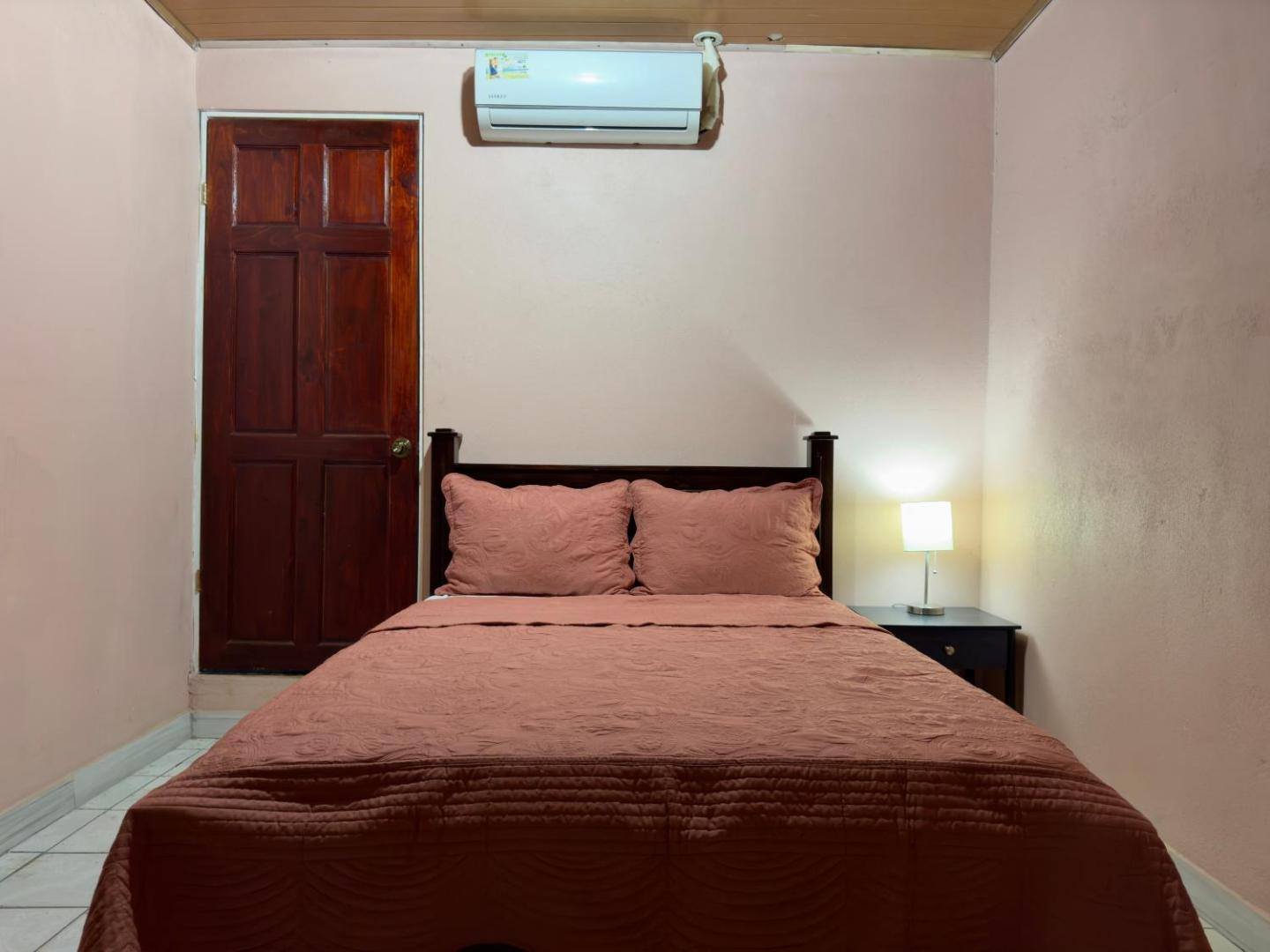A simple room with a bed, a wooden door and an air conditioner above it
